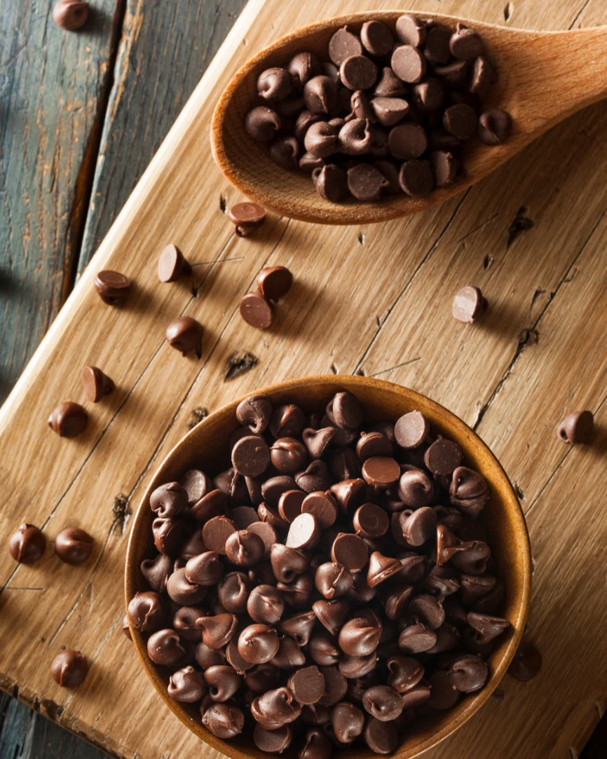 Chocolate chips in a wooden bowl and spoon on a wooden surface